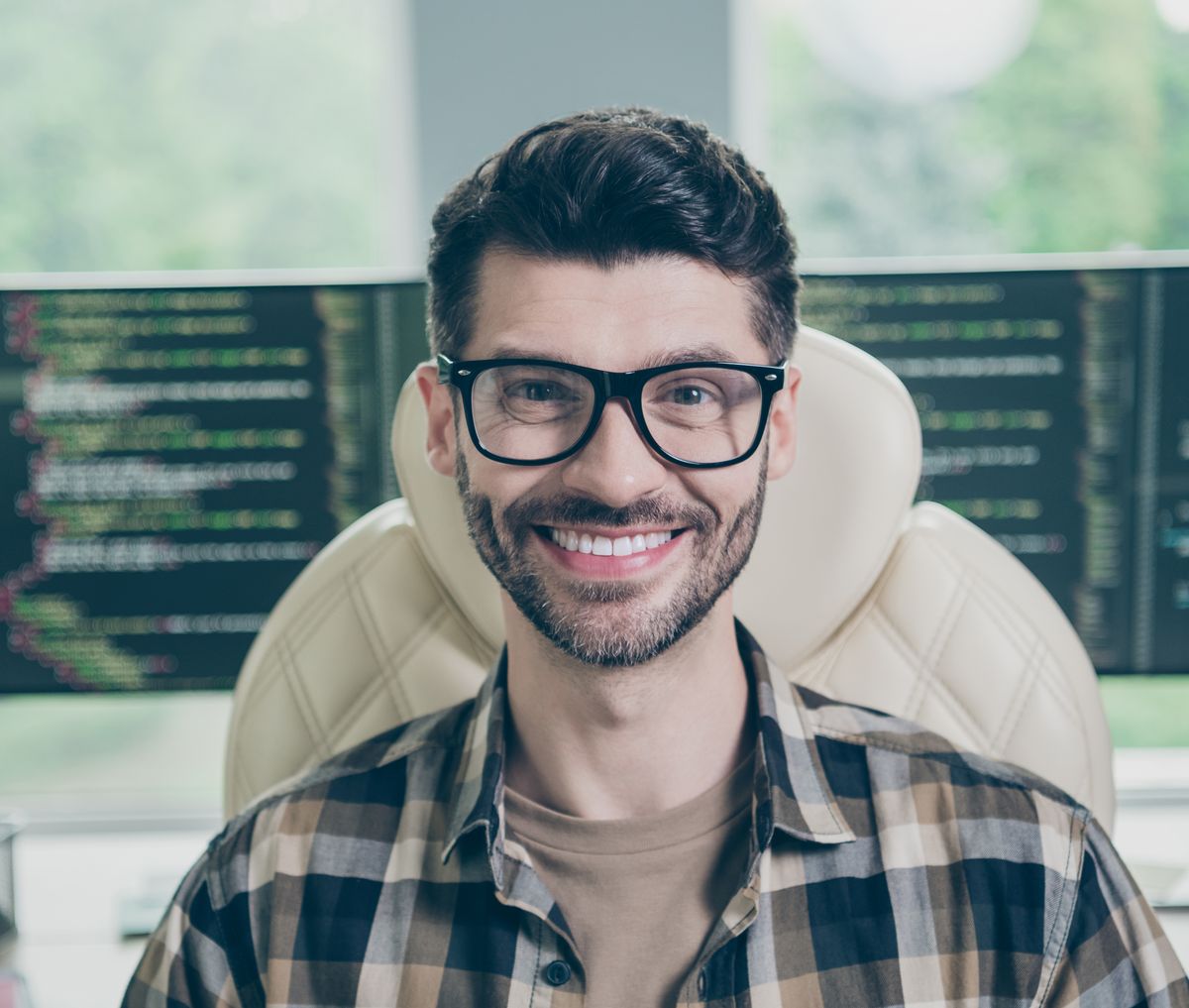 Pessoa desenvolvendo software, sorrindo, em frente a monitores com código