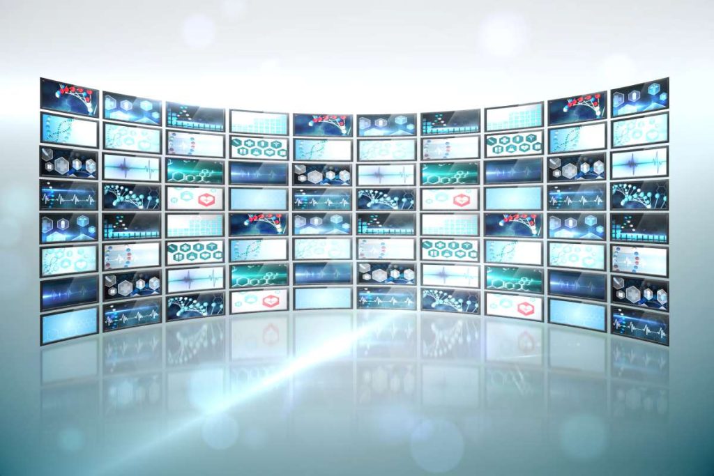A imagem retrata um NOC (Network Operations Center), com várias telas dispostas em um formato curvado, exibindo gráficos, indicadores e dados relacionados a redes e monitoramento.