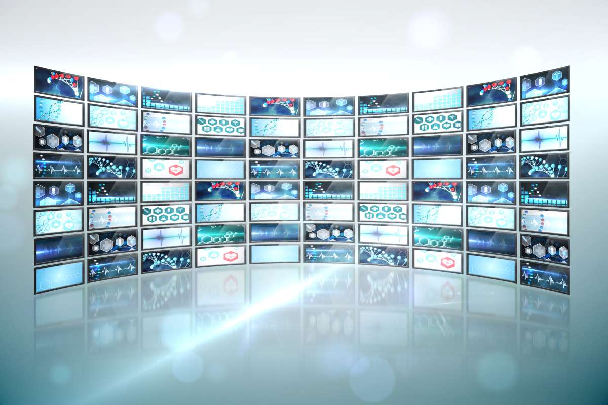 A imagem retrata um NOC (Network Operations Center), com várias telas dispostas em um formato curvado, exibindo gráficos, indicadores e dados relacionados a redes e monitoramento.