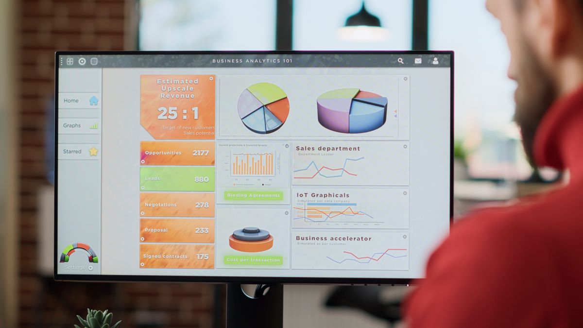 A imagem mostra um profissional observando atentamente uma tela de computador com diversos gráficos e indicadores de desempenho relacionados à área de Business Analytics.